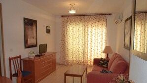 Ein Wohnzimmer mit einer Couch, einem Couchtisch, einem Fernseher auf einer Holzkommode und einer Lampe.