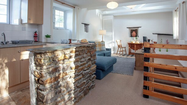 A modern kitchen with a stone island, wooden cabinets, and a dining area with a blue sofa and wooden table. - 2 bedroom accommodation in Looe (Looe)
