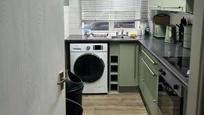 Une cuisine compacte équipée d’un lave-linge, d’une cuisinière et d’une fenêtre avec des stores.
