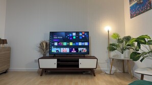 Un salon avec un téléviseur posé sur un meuble en bois, une plante en pot et un tableau accroché au mur.