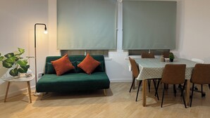 Un salon moderne avec un canapé vert, une table à manger avec des chaises et un lampadaire.