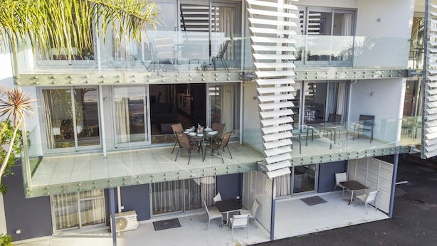 A modern two-story building with a glass balcony, outdoor seating, and a view of the surrounding area. - Paihia Beach Front 1 bedroom Apartment (Paihia)