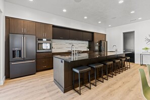 Une cuisine moderne avec des meubles en bois foncé, des appareils électroménagers en acier inoxydable, un pare-feu en marbre et un îlot central doté de tabourets de bar.