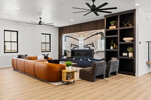 A modern living room with a sectional sofa, a flat-screen TV, a marble accent wall, and built-in shelving with decorative items. - Brand New Build! 50+ Beds (Hurricane)