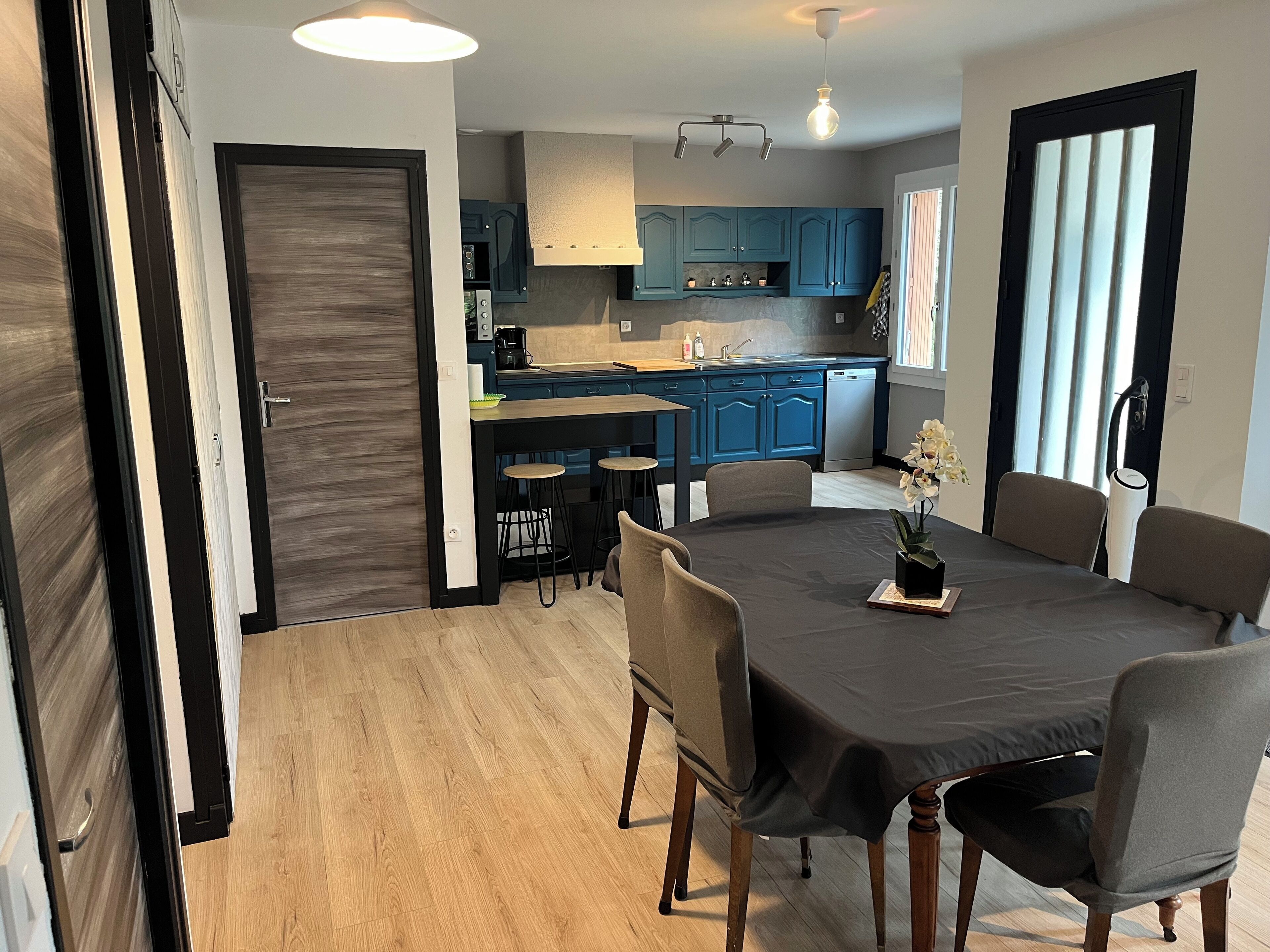 Een moderne keuken met blauwe kastjes, een eettafel met vier stoelen en een hanglamp erboven.