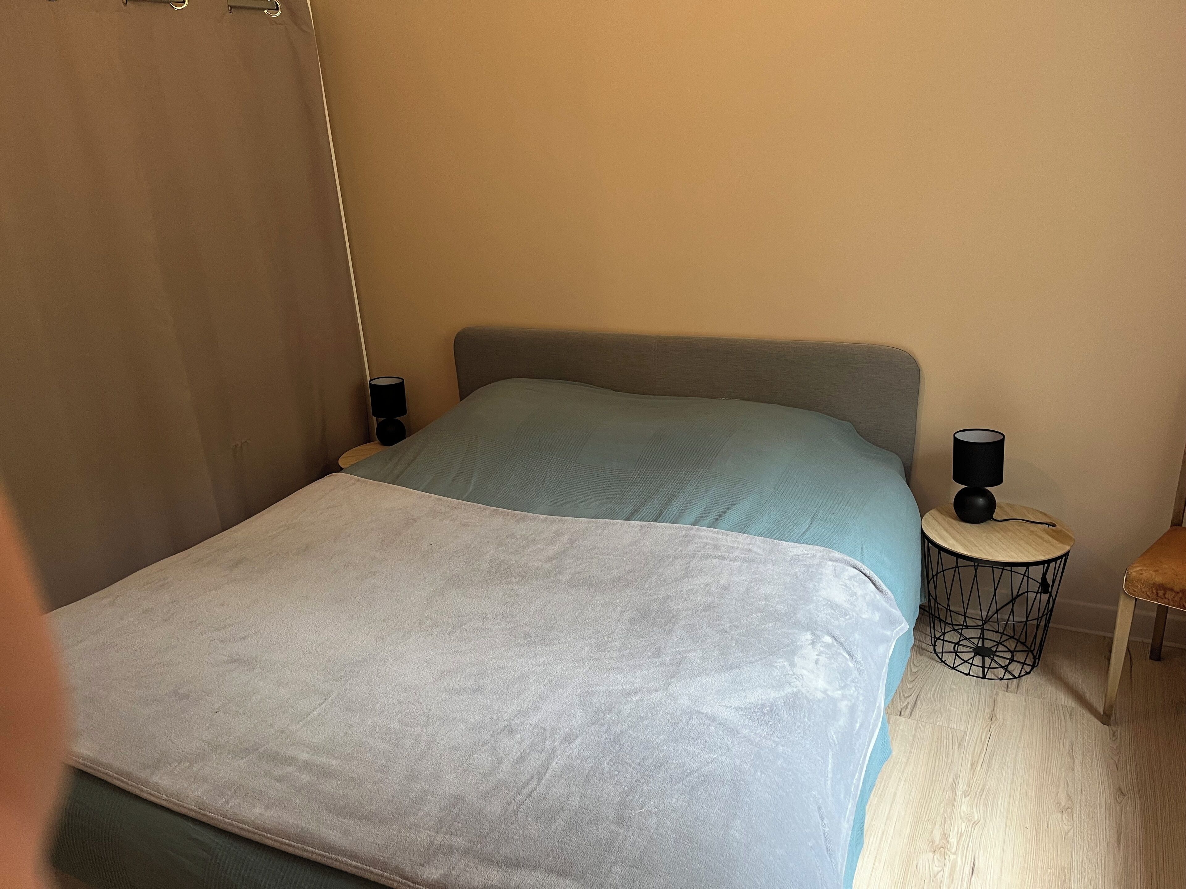 Een slaapkamer met een bed, nachtkastje, lamp en een klein tafeltje.