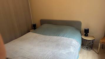 Een slaapkamer met een bed, nachtkastje, lamp en een klein tafeltje.