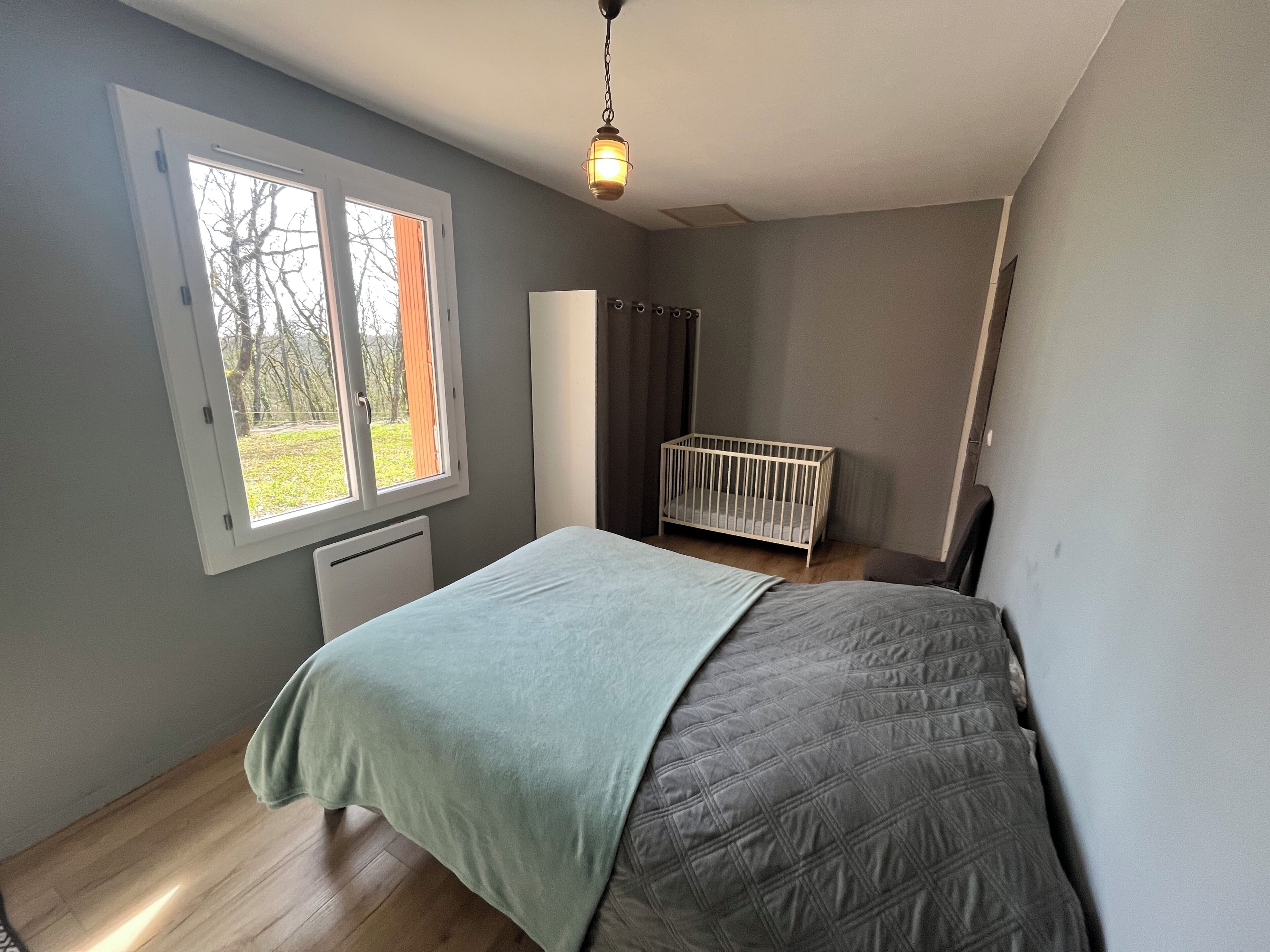 A bedroom with a bed, a crib, a window, and a radiator.
