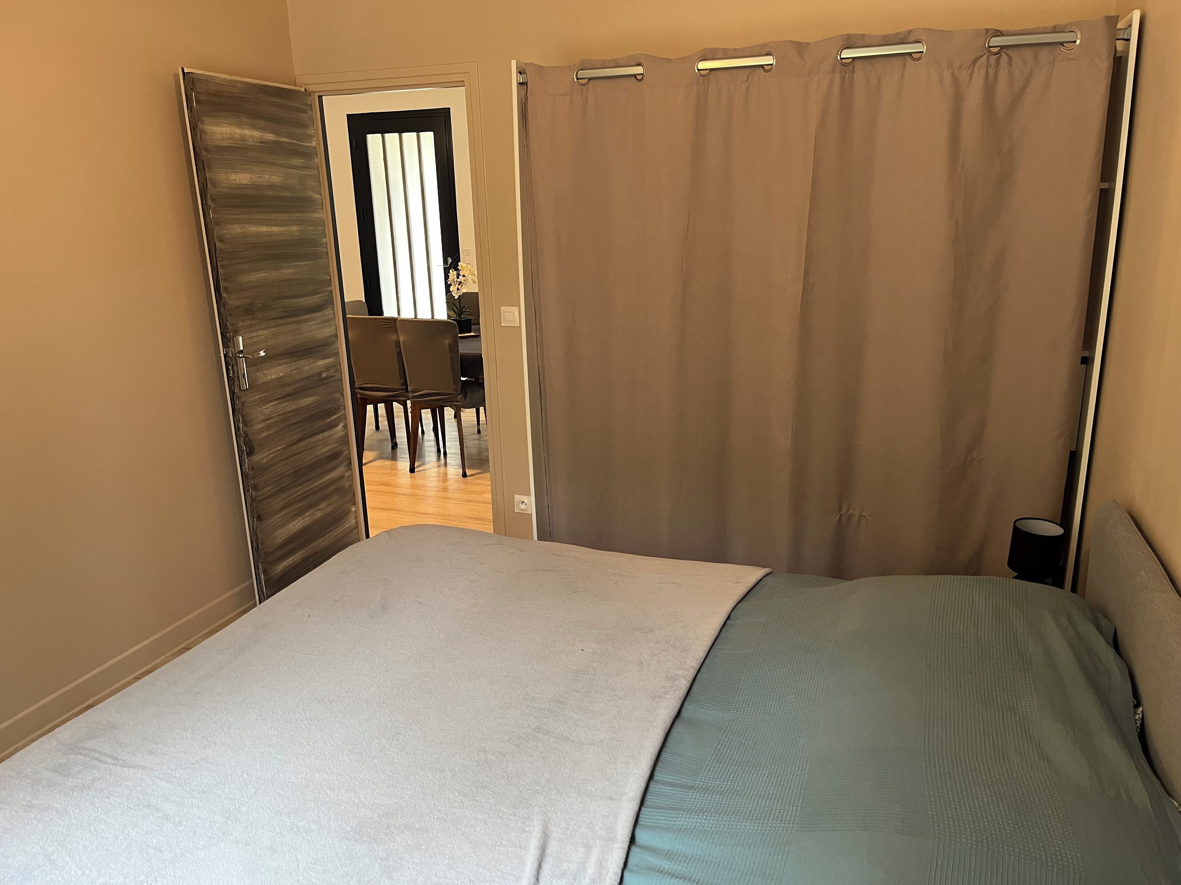 A bedroom with a bed, a door leading to a dining area, and a curtain.