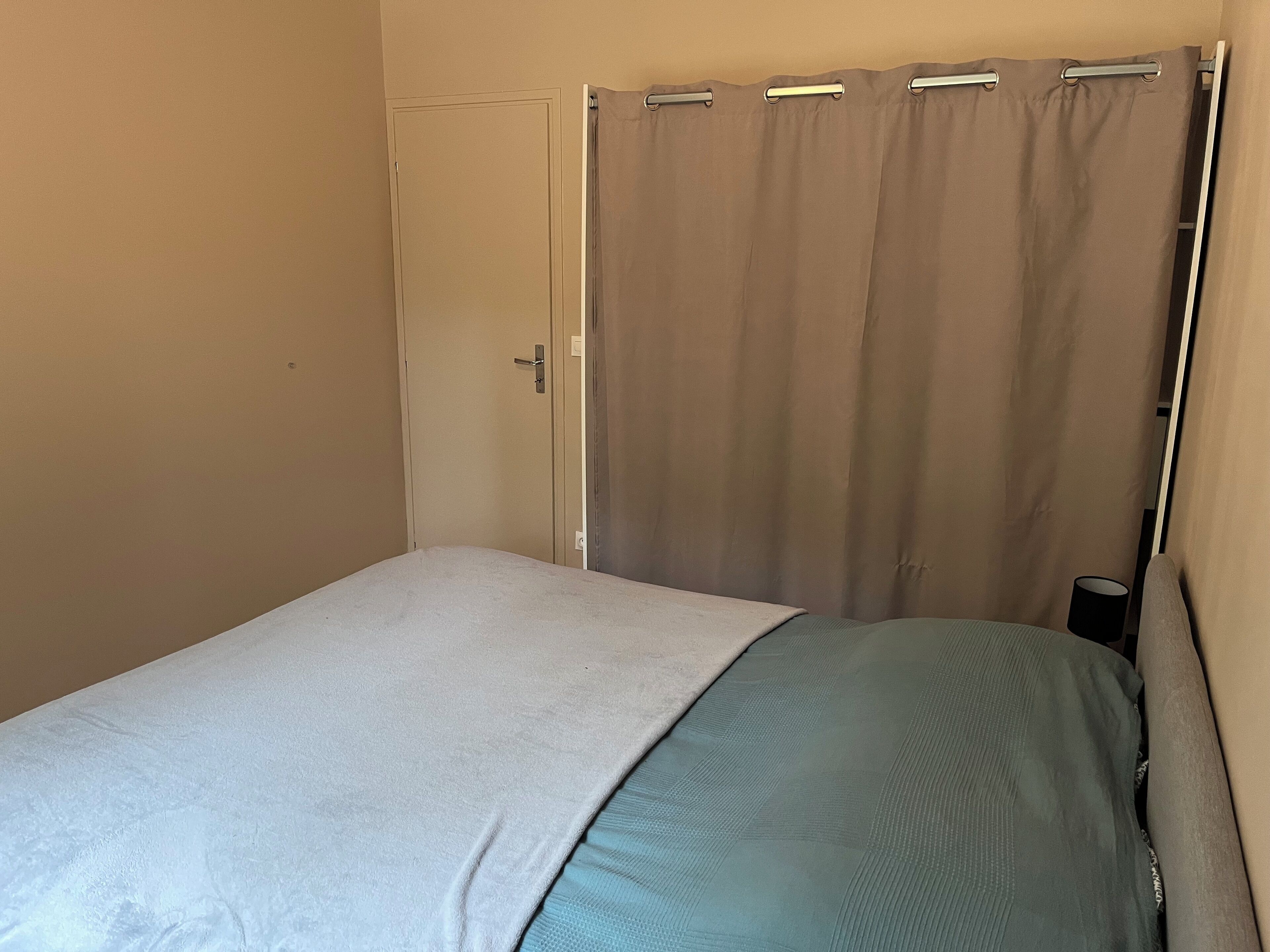 Un dormitorio con cama, una puerta y una cortina.