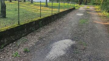 Un chemin de gravier bordé d’une clôture en fil de fer et d’arbres, qui mène à un bâtiment blanc avec une porte rouge.