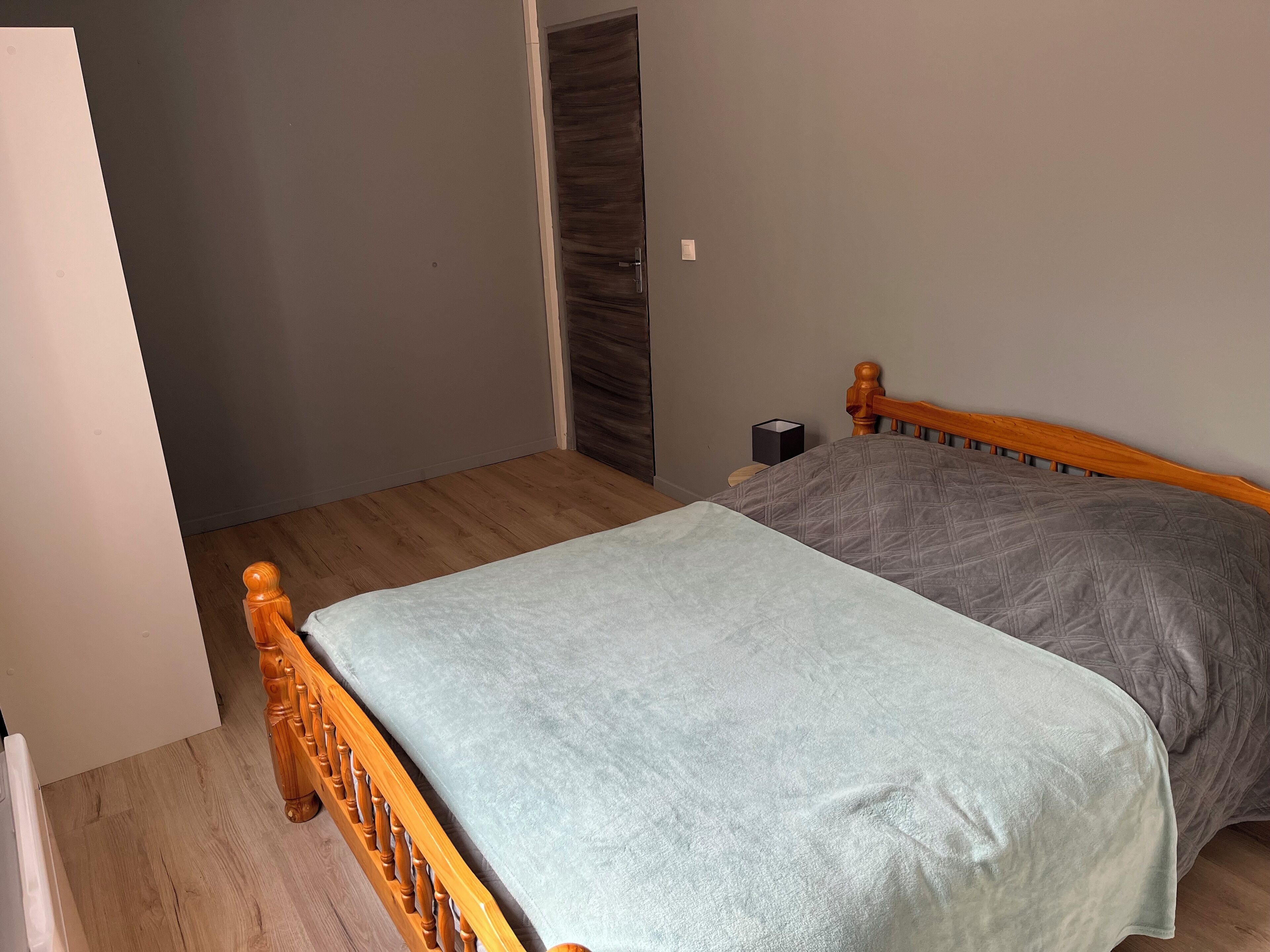 Une chambre avec un lit en bois, une couvre-lit grise et un plancher en bois.