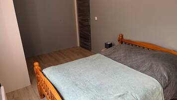 Une chambre avec un lit en bois, une couvre-lit grise et un plancher en bois.