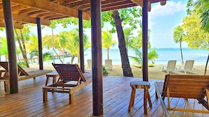 Terraza de madera con sillones de descanso con vista a una playa y al océano.