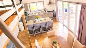 Una cocina amplia con una isla central, un comedor con una mesa redonda y una escalera que sube a un nivel superior.