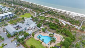 An aerial view of a resort with a swimming pool, beachfront access, and a large building.