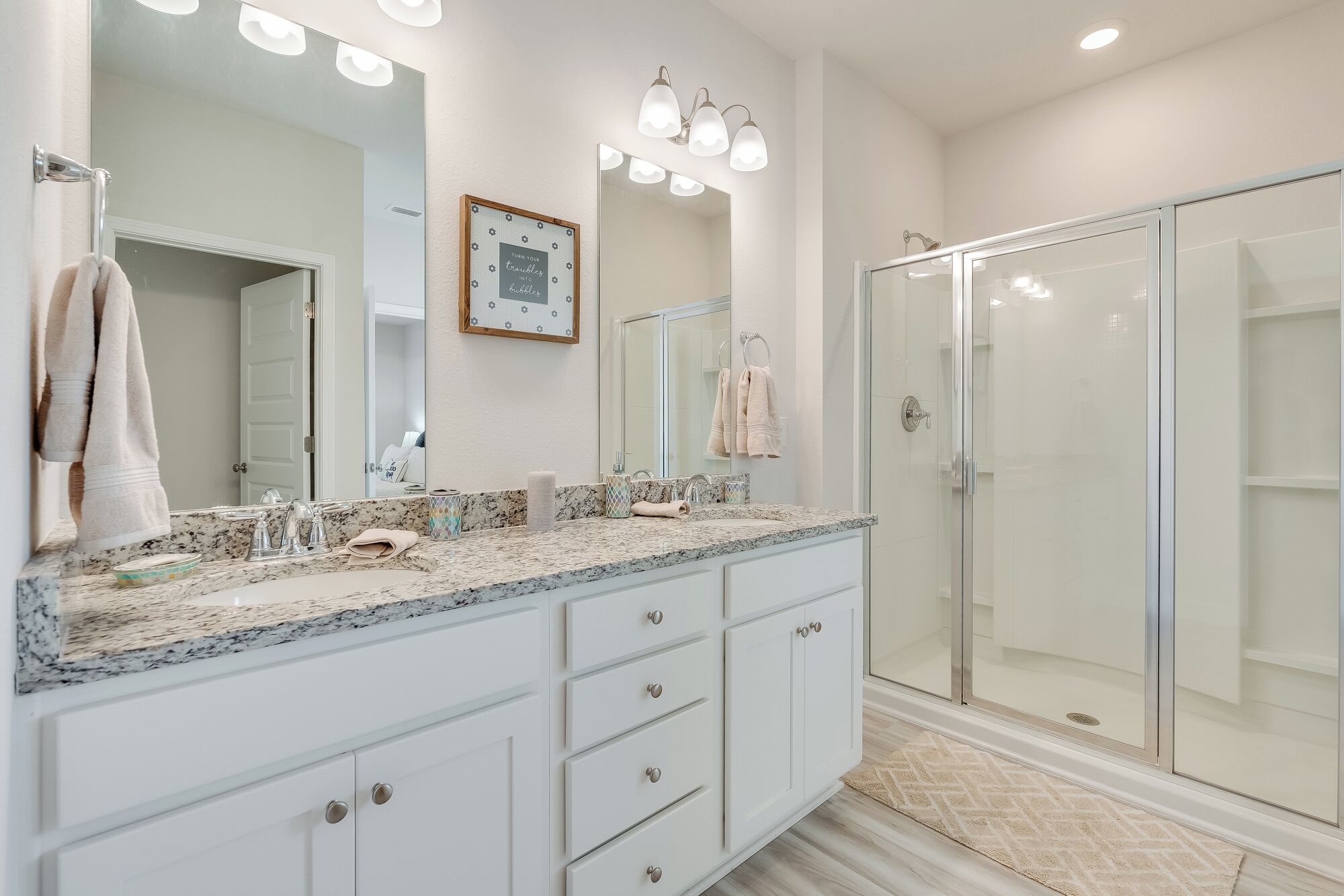 A modern bathroom with a large mirror, a glass shower enclosure, and a marble countertop.