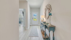 A hallway with a white door, a rustic blue console table with a lamp, and a woven basket.