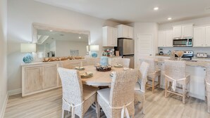 A modern kitchen with white cabinetry, a central island, and a dining area with wicker chairs.