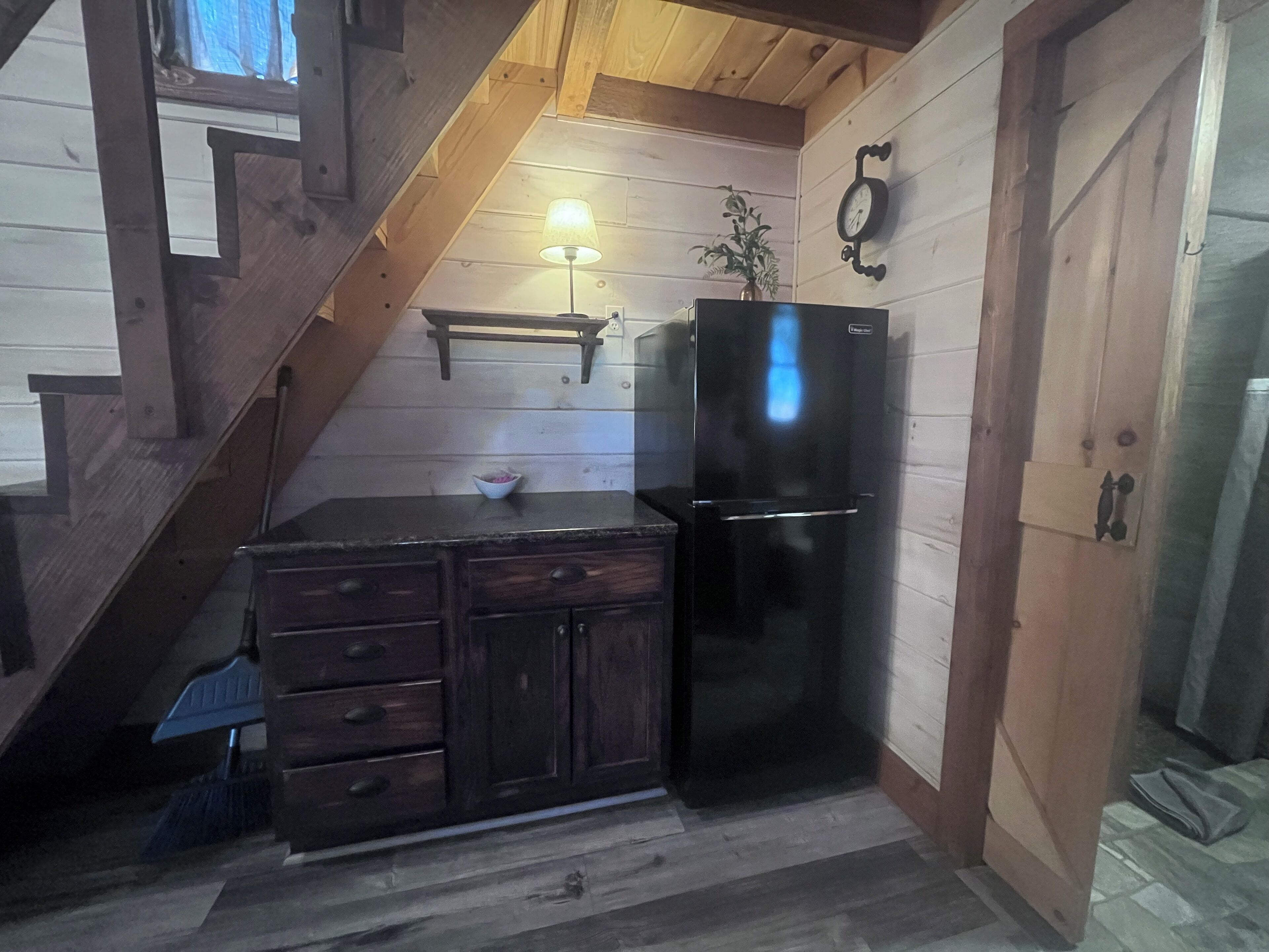 Une cuisine de taille réduite, avec un meuble en bois foncé, un réfrigérateur noir et un escalier en bois.