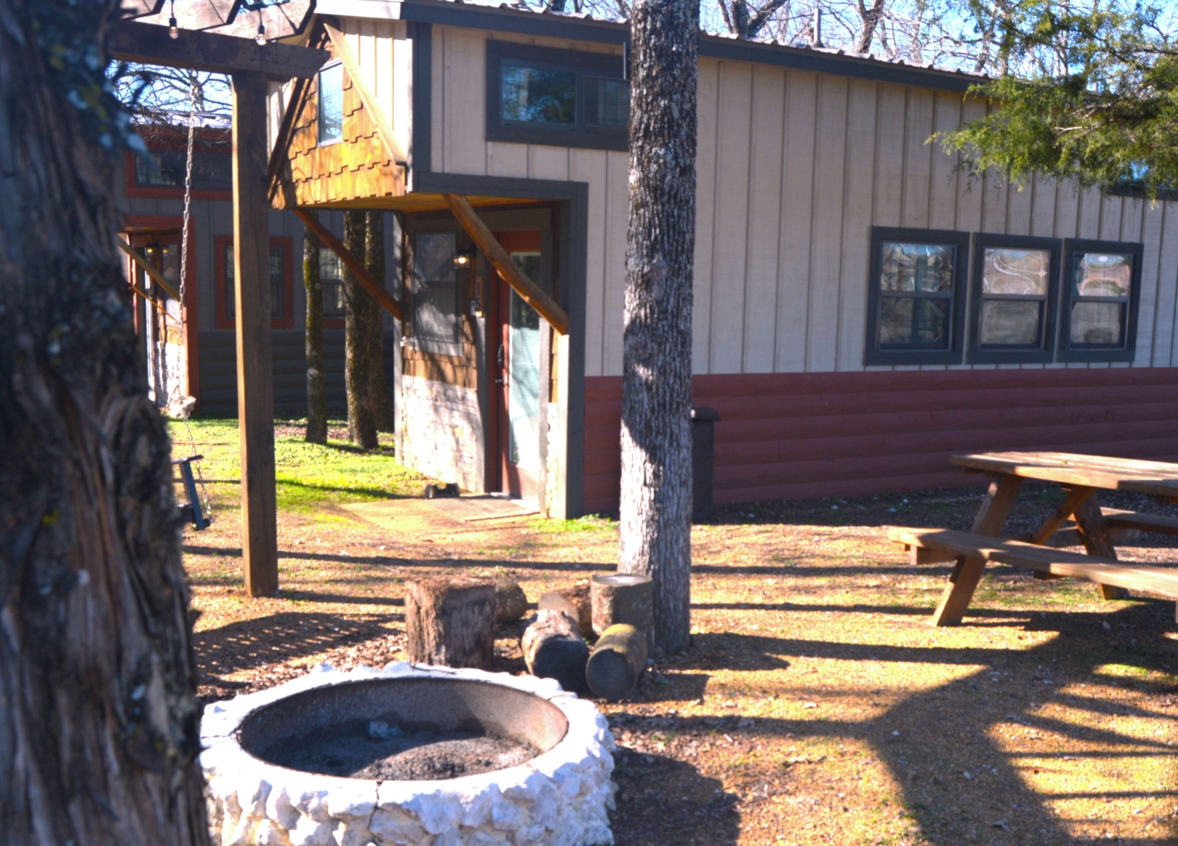 A rustic outdoor area with a wooden swing set, a picnic table, and a fire pit.