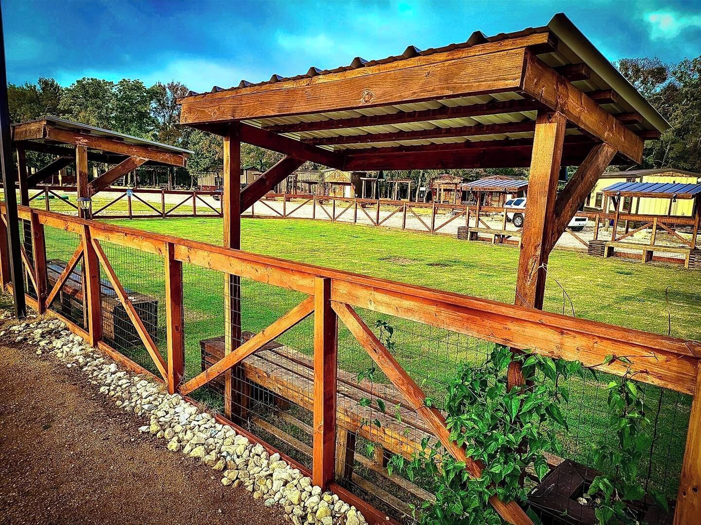 A wooden structure with a metal roof, surrounded by a gravel path and a grassy area.