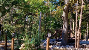 Un'area boschiva con un ponte di legno, sentieri in pietra e lanterne.