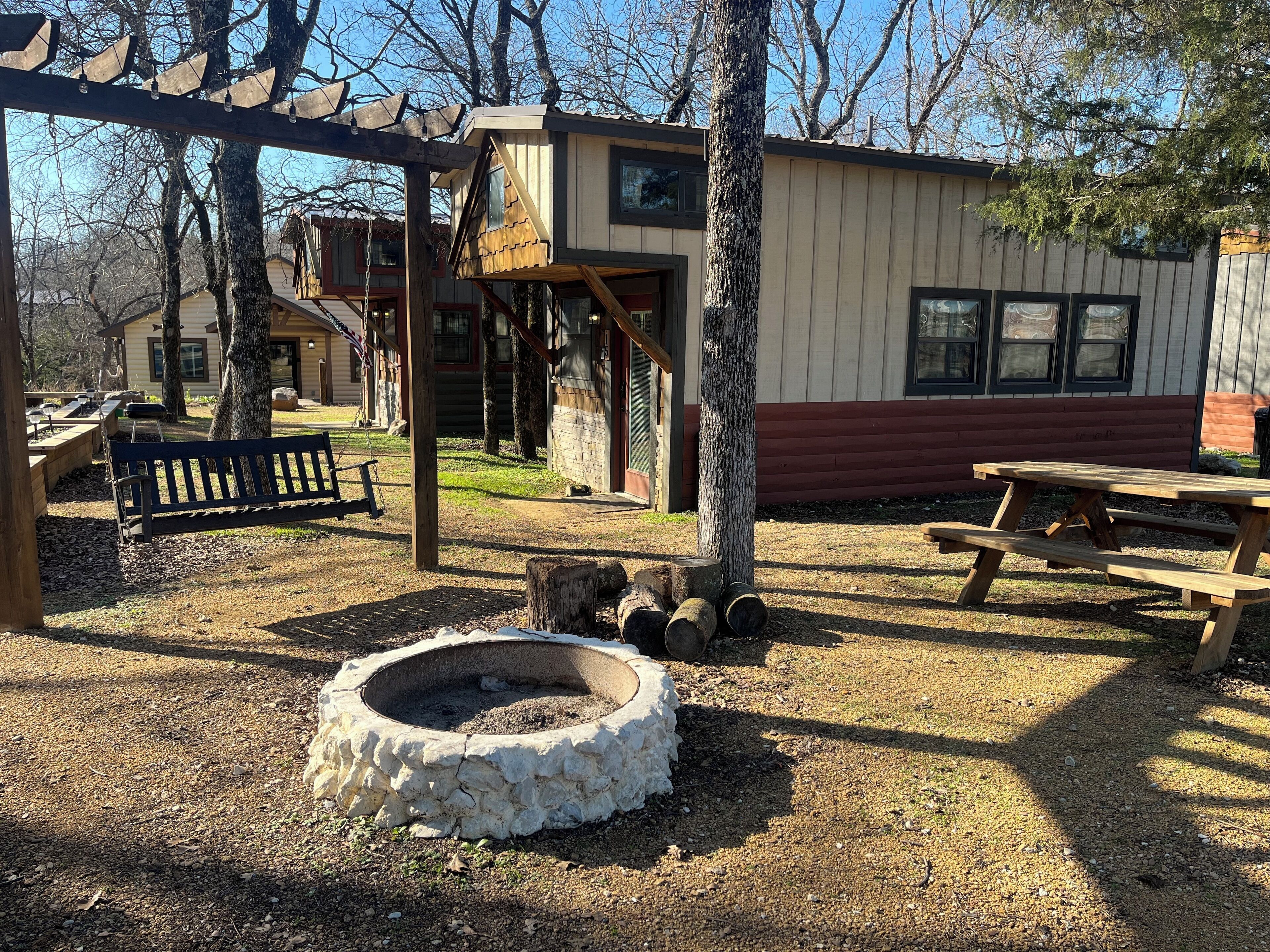 A rustic cabin with a stone fire pit, wooden benches, and picnic tables.