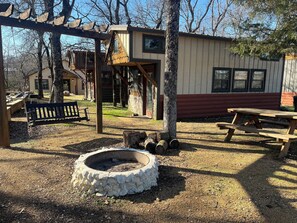 A rustic cabin with a stone fire pit, wooden benches, and picnic tables. - Tiny Home Resorts (Denison)