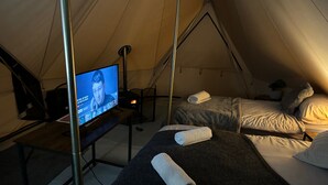 Eine Zelteinrichtung mit zwei Betten, jedes ausgestattet mit einem zusammengerollten Handtuch, einem Fernseher auf einem Tisch und einem kleinen Tisch mit einer Lampe.