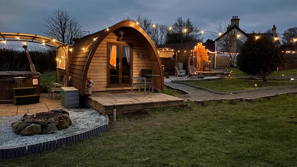 Eine gemütliche, halboffene Holzhütte mit Veranda, Feuerstelle und Lichterketten.