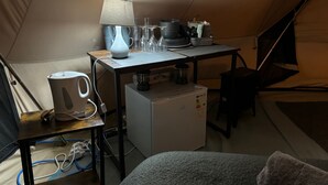 Ein Zelt mit Tisch, Lampe, Wasserkocher, Kühlschrank und verschiedenen Geschirr.