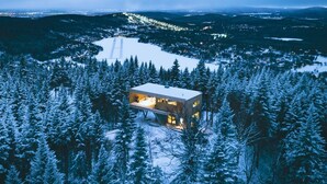 Een moderne houten hut in een besneeuwd bos met een helder uitzicht op het omliggende landschap.