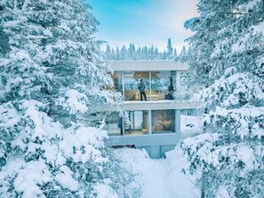 Une maison moderne en verre, entourée d’arbres couverts de neige.