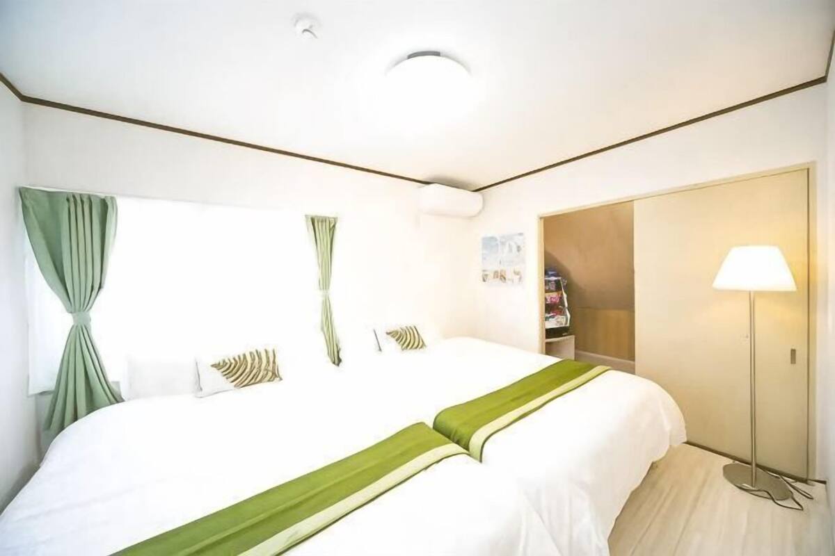 Una habitación de hotel con una cama grande, un armario, una lámpara de noche y una ventana con cortinas.