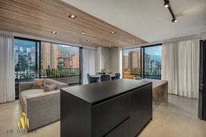 A modern living room with a large window, a sofa, a dining table, and a kitchen area. - Morph 1602 - Luxurious Retreat in Poblado/Jacuzzi/Air Conditioning (Medellín)