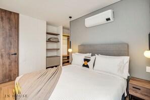 A modern hotel room with a large bed, built-in wardrobe, and a wall-mounted air conditioner.