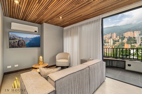 A modern living room with a large window, a sofa, a chair, and a mounted TV.