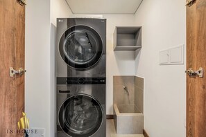 A laundry room with two stacked washers and dryers, a small shelf, and a shower area.