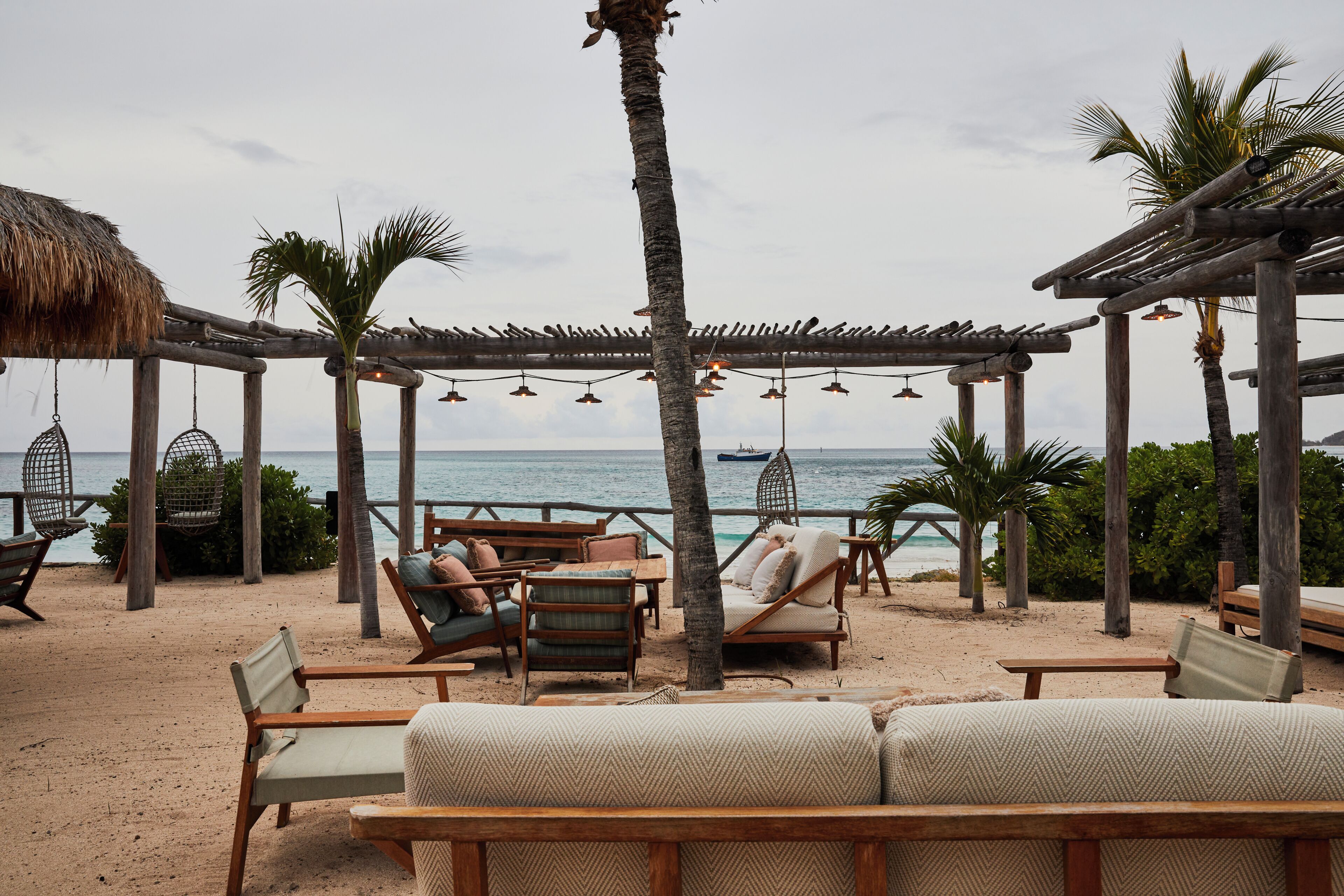 Un salon de plage doté de meubles en bois, de fauteuils suspendus et offrant une vue sur l’océan.