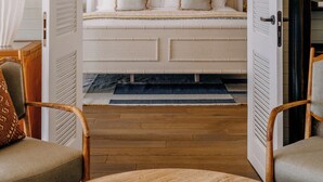 A room with a bed, two chairs, a wooden floor, and a wall with a woven basket. - Soho Beach House Canouan (Canouan Island)