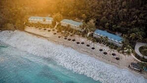 An aerial view of a beachfront hotel with multiple buildings, a sandy beach, and palm trees. - Soho Beach House Canouan (Canouan Island)