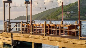A wooden pier with a sign reading 'SOHO BEACH HOUSE,' tables with chairs, and a string of lights. - Soho Beach House Canouan (Canouan Island)
