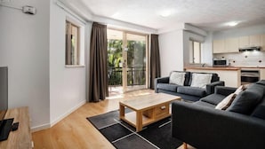 A modern living room with a sofa, coffee table, and a TV. There is a sliding glass door leading to a balcony. - Turtle Beach Resort (Mermaid Beach)
