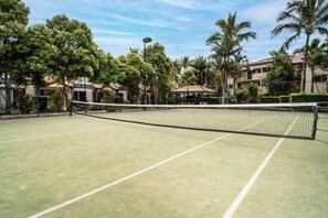 A tennis court with a net, surrounded by trees and buildings. - Turtle Beach Resort (Mermaid Beach)