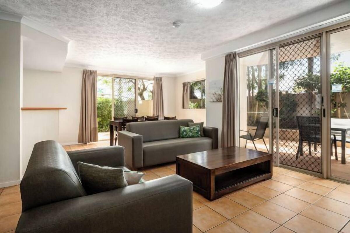A modern living room with a sofa, a coffee table, and a sliding glass door leading to an outdoor area.