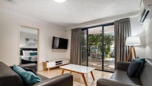 A modern hotel room with a sofa, a small table, a TV, and a sliding glass door leading to an outdoor area. - Turtle Beach Resort (Mermaid Beach)