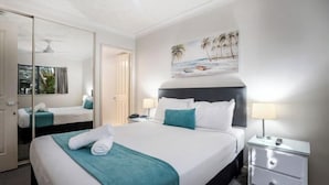 A hotel room with a large bed, a bedside table with a lamp, a mirror, and a painting of a beach scene. - Turtle Beach Resort (Mermaid Beach)