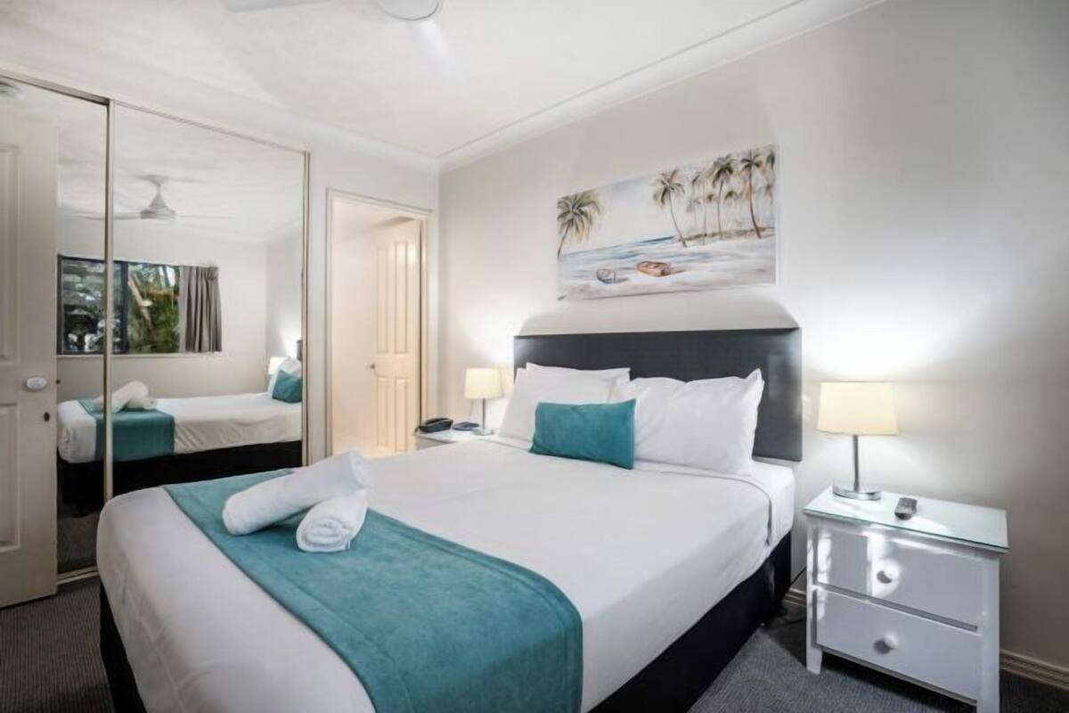 A hotel room with a large bed, a bedside table with a lamp, a mirror, and a painting of a beach scene.
