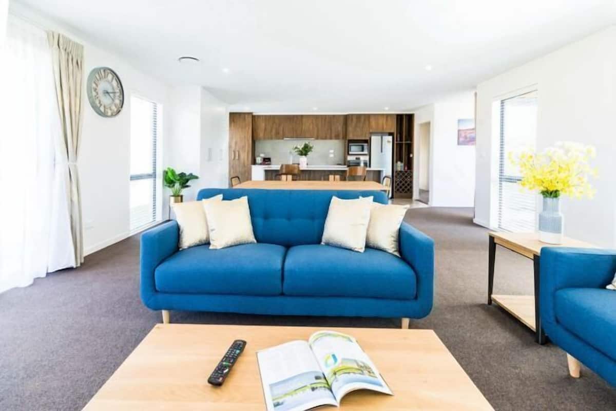 A modern hotel room with a blue sofa, a wooden coffee table, a remote control, and an open magazine.